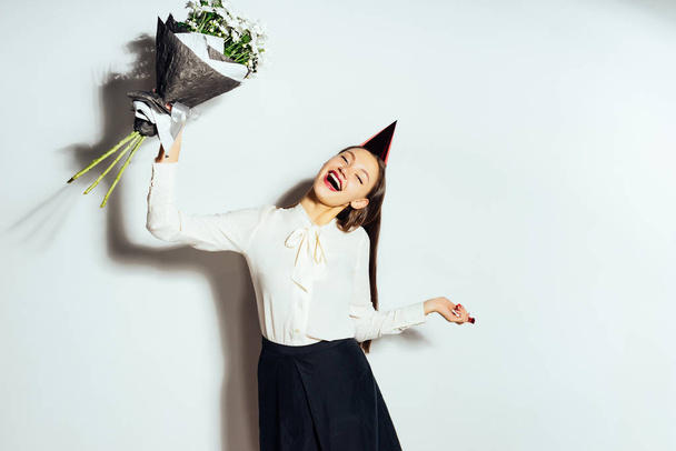 young happy girl celebrates something, in a red cap and holds a large bouquet of white flowers - 写真・画像