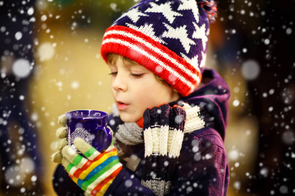 Niño bebiendo chocolate caliente en el mercado de Navidad
 - Foto, imagen