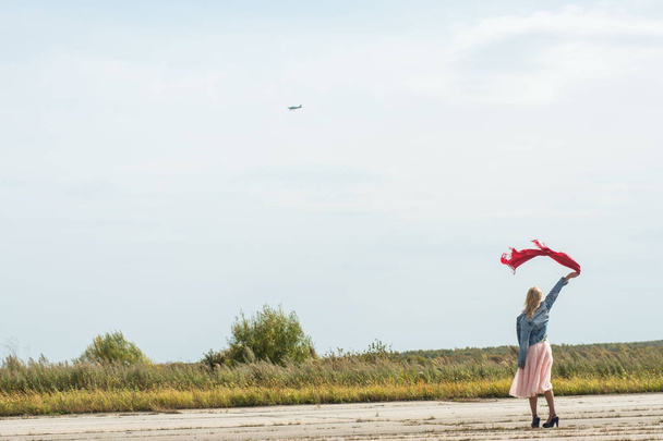 Stijlvolle slanke vrouw, zwaaien zijn hand vliegen vliegtuigen in zonnige zomerdag. Reizen, vakantie, concept van avonturen. - Foto, afbeelding