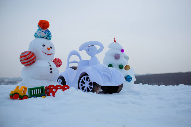 Snowman and toy car on snowy background - Fotoğraf, Görsel