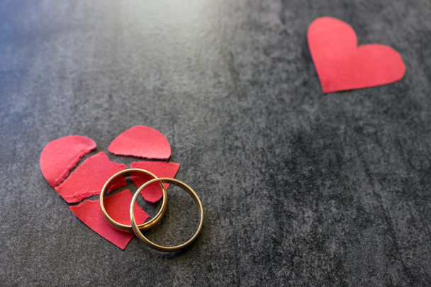 Anéis de casamento e coração vermelho partido. Fundo preto. A concha
 - Foto, Imagem