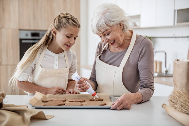 Cheerful girl baking holiday sweet food with granny - 写真・画像