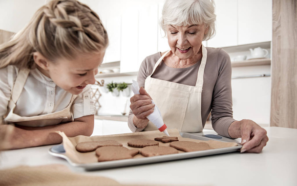 Feliz abuela apretando crema en las galletas de vacaciones
 - Foto, Imagen