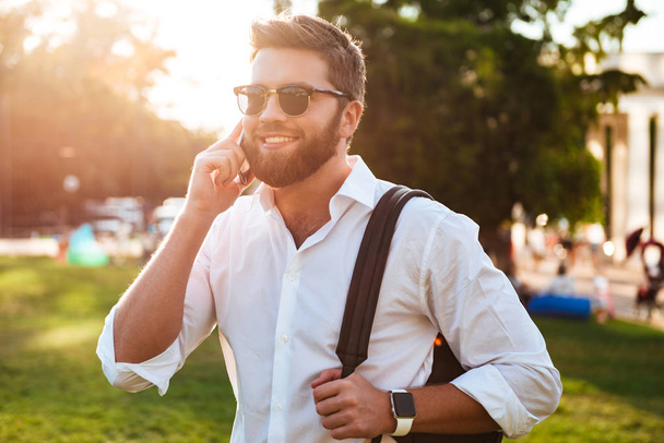 Happy bearded man in sunglasses standing outdoors while holding backpack - Foto, immagini