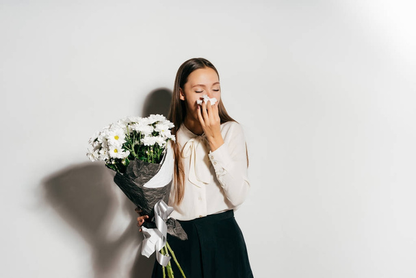 a beautiful young girl sneezes because she is allergic to the flowers she keeps in her hands - Foto, Bild