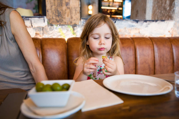 bambina in ristorante guardando l'oliva in mano
 - Foto, immagini