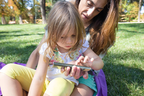 petite fille touchant écran mobile de la femme assise dans le parc
 - Photo, image