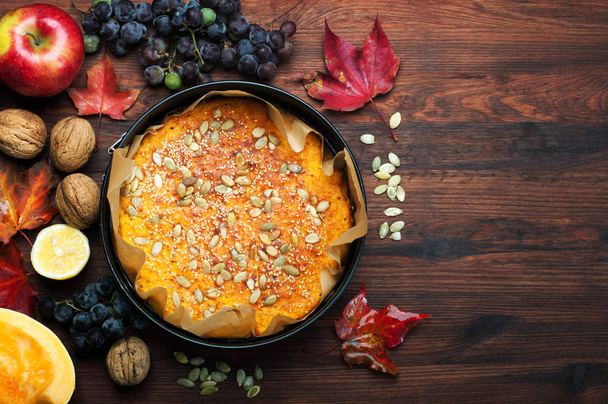 Juicy yellow pumpkin pie decorated with pumpkin seeds and sesame seeds against the background of autumn foliage, apples, nuts and grapes. Autumnal seasonal menu. Vegetarian concept - Foto, Imagem
