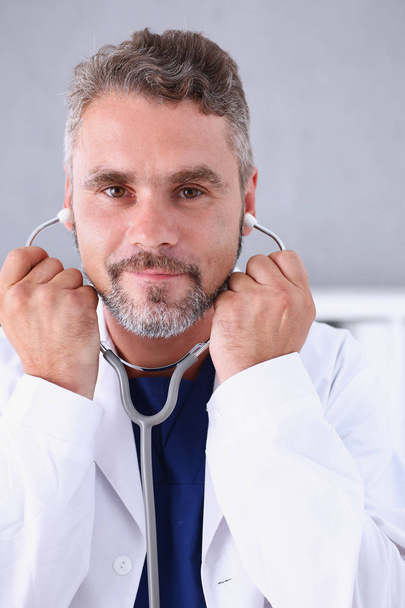 Handsome mature smiling male doctor hold in arms stethoscope - Foto, Imagen