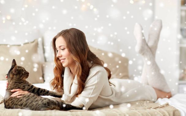 happy young woman with cat lying in bed at home - Foto, Imagen