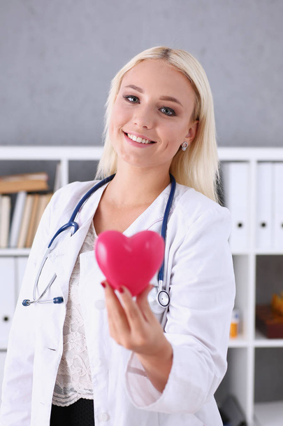 Όμορφη χαμογελαστή γιατρός κρατήστε στα χέρια κόκκινη καρδιά - Φωτογραφία, εικόνα