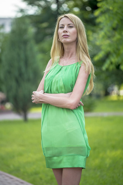  Beautiful blonde girl in a green short summer dress on the streets of the city - Foto, immagini