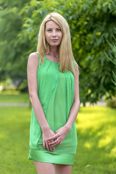  Beautiful blonde girl in a green short summer dress on the streets of the city - Valokuva, kuva