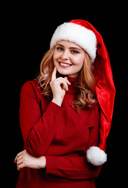 Beautiful happy festive girl in a santa cap on a black background. Christmas costume concept. - Foto, imagen