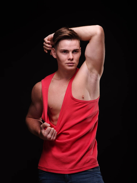 Healthy, beautiful, young man pulling his red t-shirt on a black background. Sporty lifestyle concept. - Fotografie, Obrázek