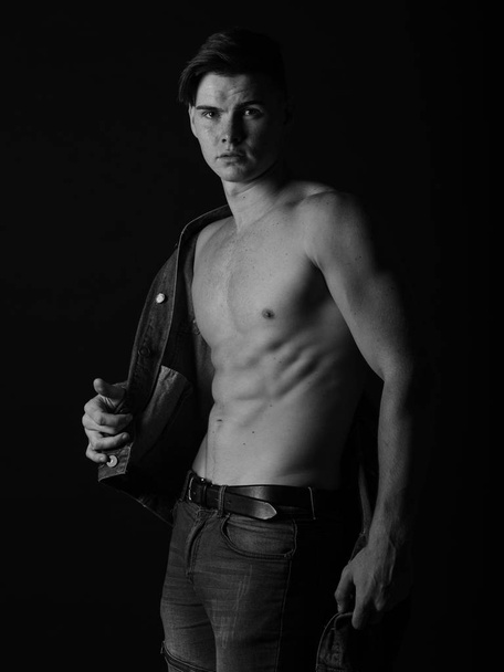Gorgeous fit man in a jeans jacket, shirtless on a black background. Black and white sexy man concept. - Foto, immagini