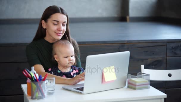 Mosolygó nő és baba ül az asztalnál, és keresi, hogy a képernyő a laptop. - Felvétel, videó