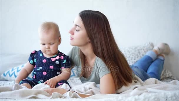 Kobieta o długich ciemnych włosach jest Całowanie córki niemowlę, leżące w sypialni. - Materiał filmowy, wideo