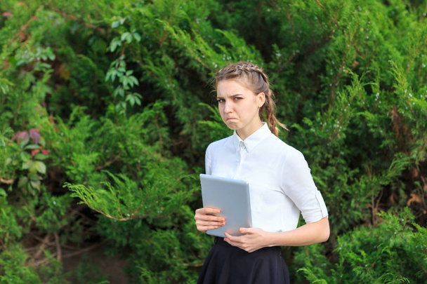 A young brunette girl sits in a park with a tablet. - Photo, Image