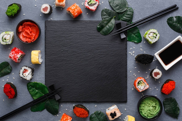 Placa cuadrada de pizarra negra con sushi sobre fondo gris rústico, espacio para copiar
 - Foto, Imagen