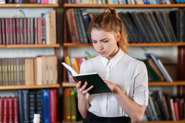 Retrato de una joven que está leyendo un libro en la biblioteca
. - Foto, Imagen