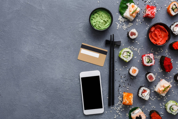 Widok z góry zestaw sushi roll i gunkan w pobliżu telefonu i karty kredytowej na rustykalny szary i ryż tło - Zdjęcie, obraz