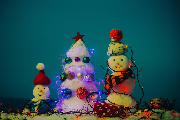 Gratulálok neked, karácsony és újév. Vidám érzelmek a hó szobrászat. Üdvözlőlap család. Hó szobrok rajta sapka, kabát és sál. Karácsonyfa és a hóemberek borított garland - Fotó, kép