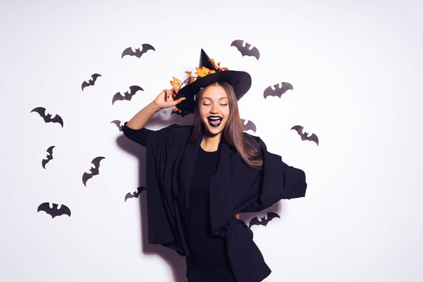 young sexy gothic girl in the shape of a witch in halloween, in a big black hat, posing against the wall and laughing - Fotoğraf, Görsel