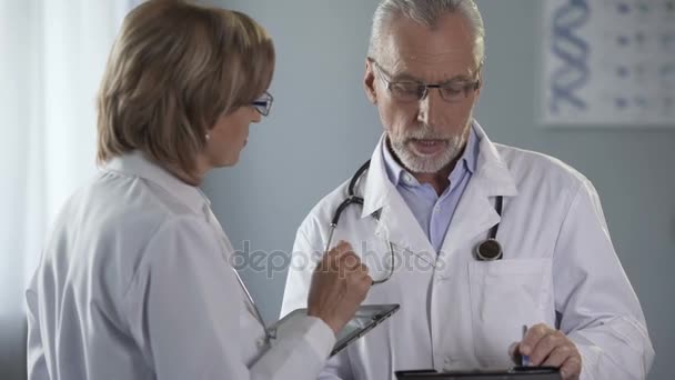 Ärzte diskutieren über Ergebnisse, Frau hält Tablet, Mann Notizblock - Filmmaterial, Video