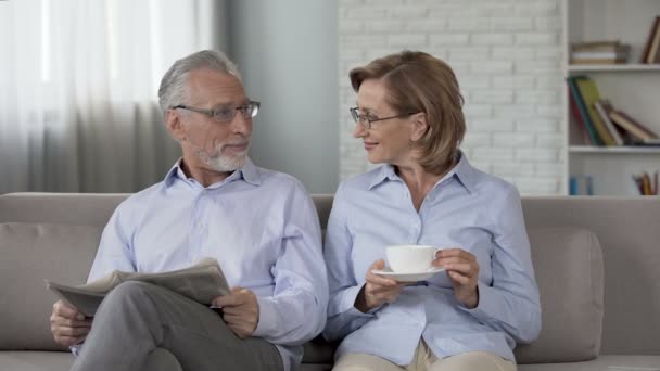 Aged couple sitting on couch, man reading newspaper, woman enjoying tea, advert - Filmmaterial, Video