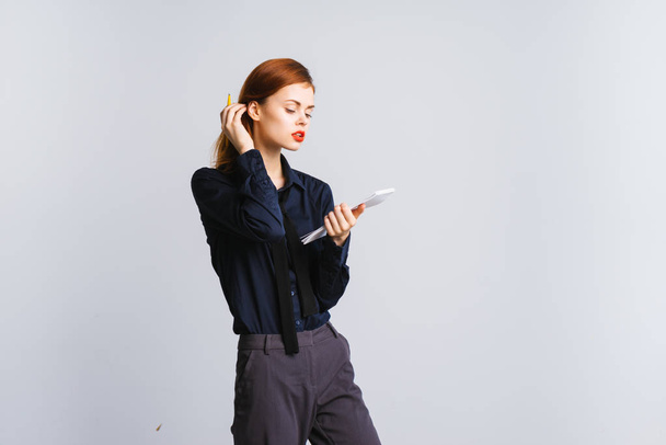 sexy red-haired girl in dark blue shirt is holding a folder with papers and wants something to write down there, isolated on white background - Zdjęcie, obraz