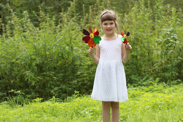 Pretty little girl with two windmills smiles in summer green for - 写真・画像