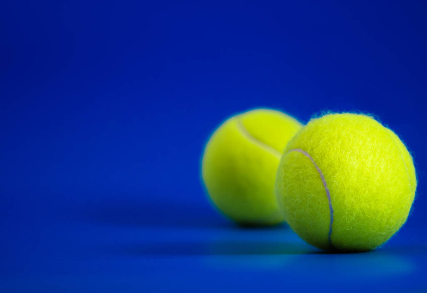 dos nuevas pelotas de tenis en pista azul con luz de la derecha, sombra y espacio de copia a la izquierda
 - Foto, Imagen