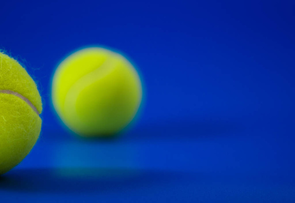 two new tennis balls on blue court with light from left, shadow and copy space on right - Photo, Image