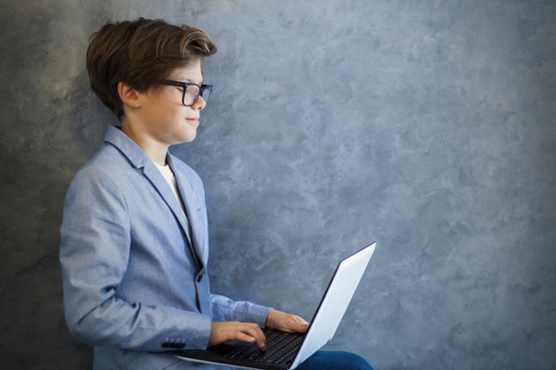 Teini poika yllään lasit istuu ja käyttää kannettavaa tietokonetta
 - Valokuva, kuva