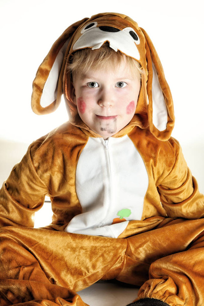 Маленький хлопчик, одягнений для кролика, сидить на землі
 - Фото, зображення