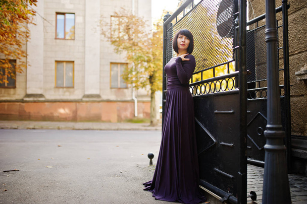 Adult brunette woman at violet gown background black iron gates. - Fotó, kép