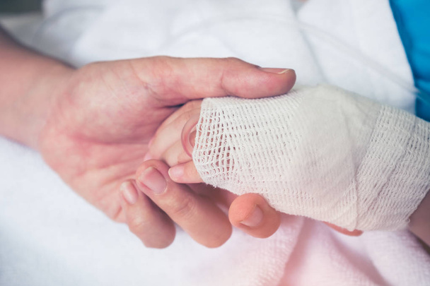 Κλείστε το χέρι του γονέα, κρατώντας το χέρι του παιδιού στο νοσοκομείο.  - Φωτογραφία, εικόνα