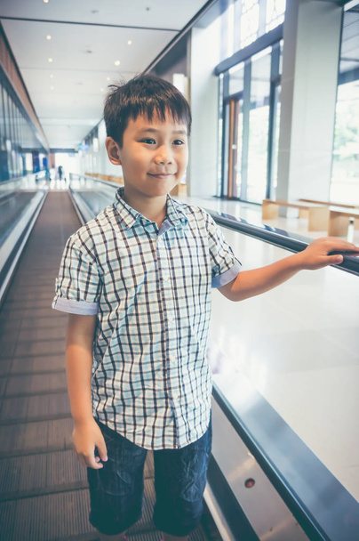 立っていると近代的な空港での電気 speedwalk の笑顔幸せなアジアの子. - 写真・画像