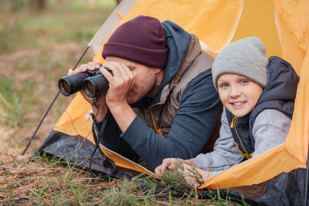 father and son with binoculars in tent - Photo, Image