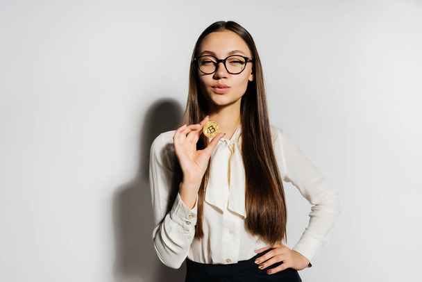 young successful confident woman with glasses holds a gold bitcoin in her hand - Photo, image