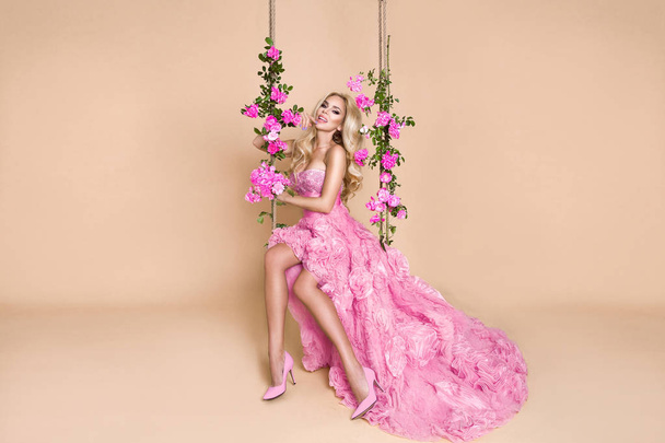 Beautiful blonde bride in a wedding dress on a swing decorated with roses - Foto, imagen