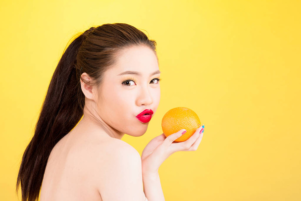 Young Asian woman kissing orange isolated in yellow background. - Valokuva, kuva
