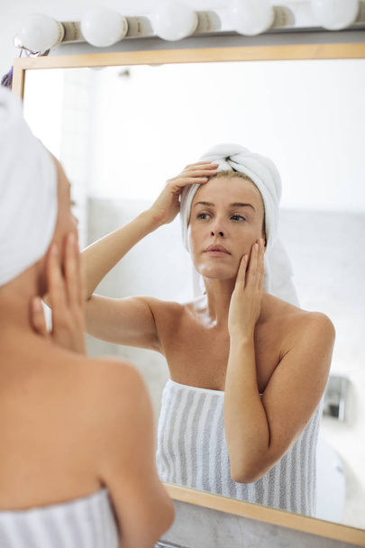 Woman Looking Herself in Bathroom Mirror - Фото, изображение