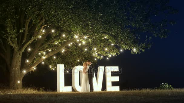 Jovem casal apaixonado em vestidos de noite estão dançando perto de cartas de luz do amor
. - Filmagem, Vídeo