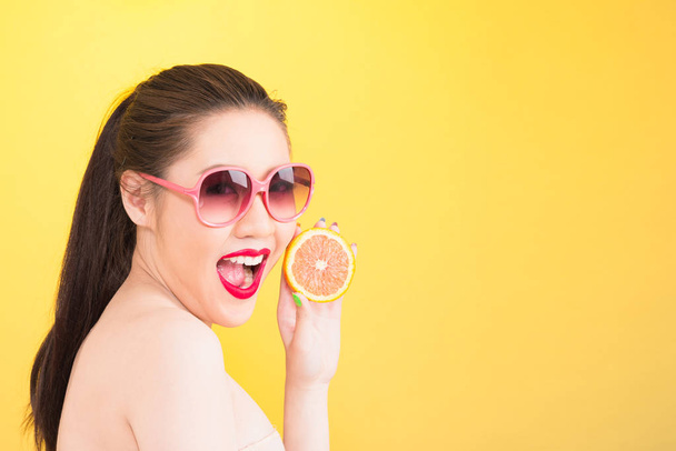 Young Asian woman holding orange isolated in yellow background. - 写真・画像