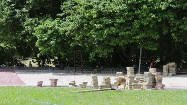 Männer verlegen dekorative bunte Pflastersteine in einem Kinderpark und reparieren Gehwege. Arbeiter beim Verlegen einer Pflasterplatte. Verlegung farbiger Fliesen im Stadtpark. Hand befestigte tessellated Gehwegfliese - Filmmaterial, Video