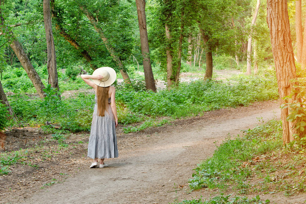 Girl in a hat is standing in a forest on a path in the forest. Back view - Foto, Imagem
