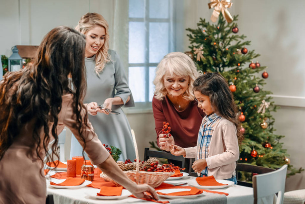 women decorating christmas table with girl - Foto, Bild