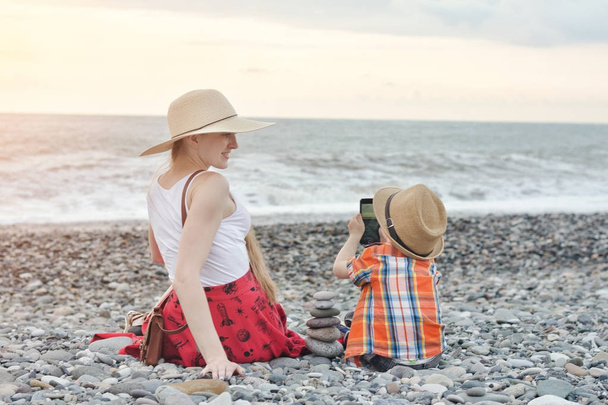 El niño fotografía a su madre en el teléfono, costa del mar
 - Foto, Imagen